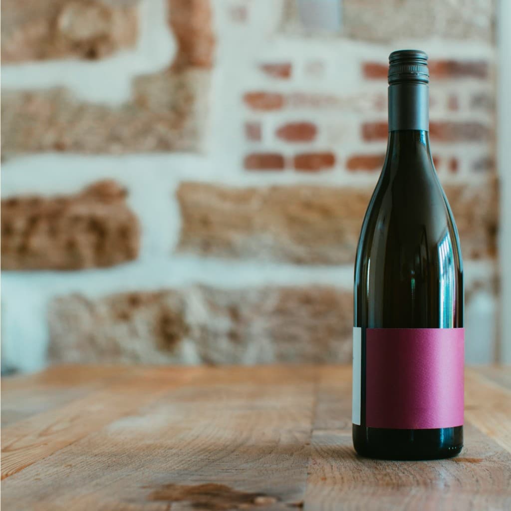 A bottle of red wine on a wooden table against an exposed brick wall